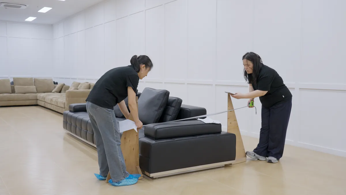 Two people inspect a sofa with a measuring tape.