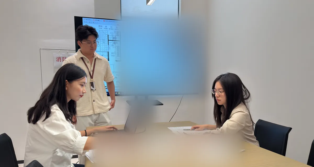 Three team members review drawings at a meeting table.