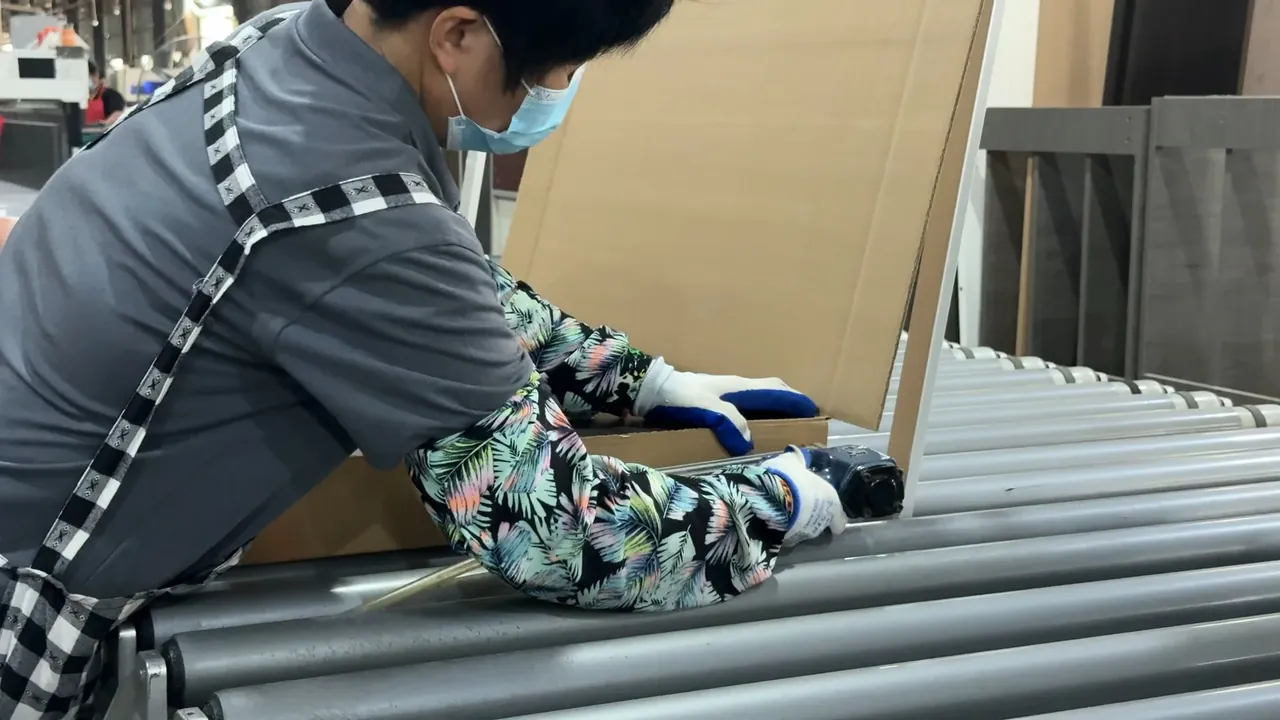 A worker wearing gloves tapes a cardboard package on a roller conveyor.