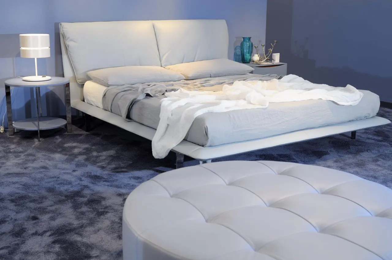 A low pale upholstered bed with a wide headboard in a bedroom setting.