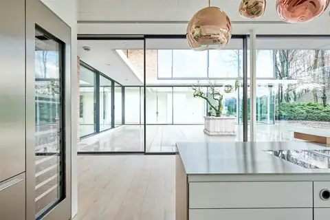 A light-filled kitchen and living space with tall glazed openings and slender dark frames.