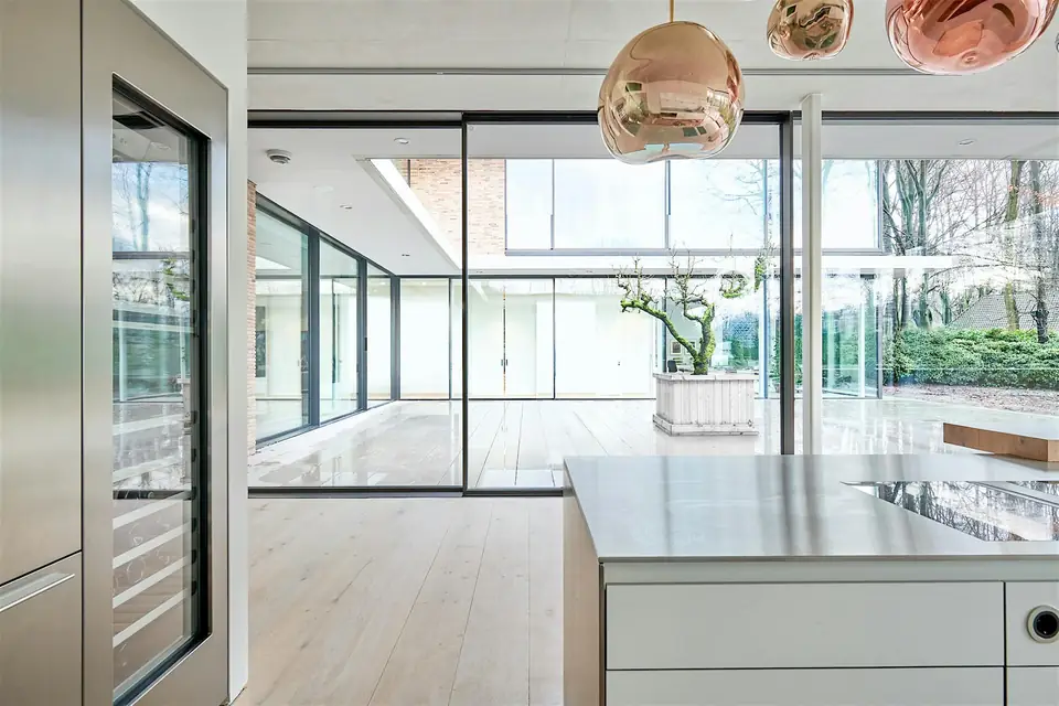 A light-filled kitchen and living space with tall glazed openings and slender dark frames.