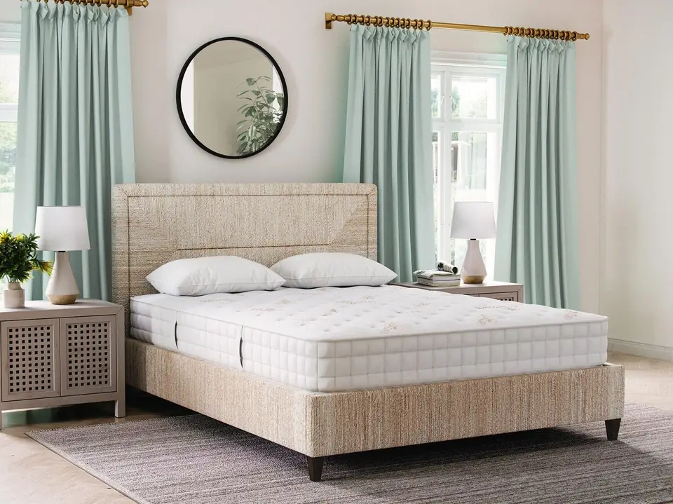 A made bed with a visible white mattress and woven headboard in a softly lit bedroom.