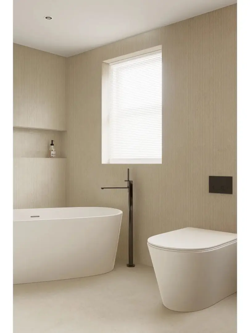 A pale bathroom with wall and floor surfaces surrounding a freestanding bathtub.