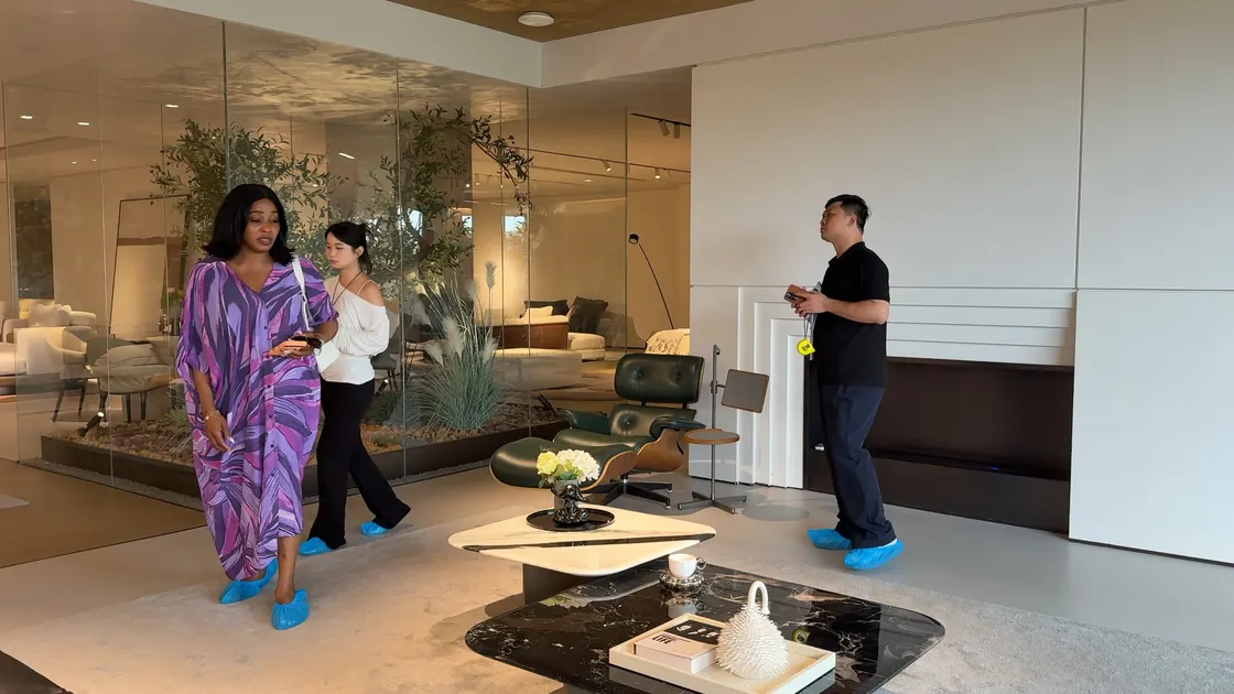 Three adults stand in a living-room furniture display with lounge chairs and coffee tables.