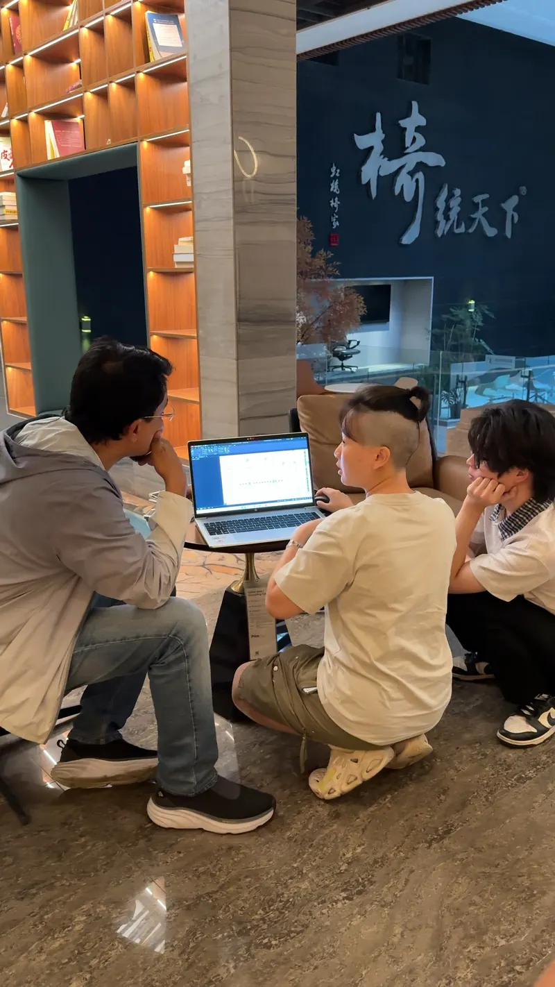 Three people gather around an open laptop on a small table.