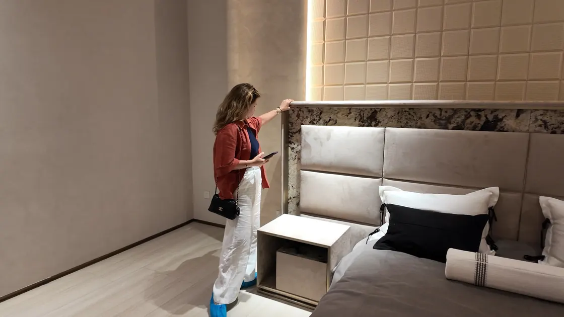 A person touches the top edge of a bed headboard in a showroom bedroom setting.
