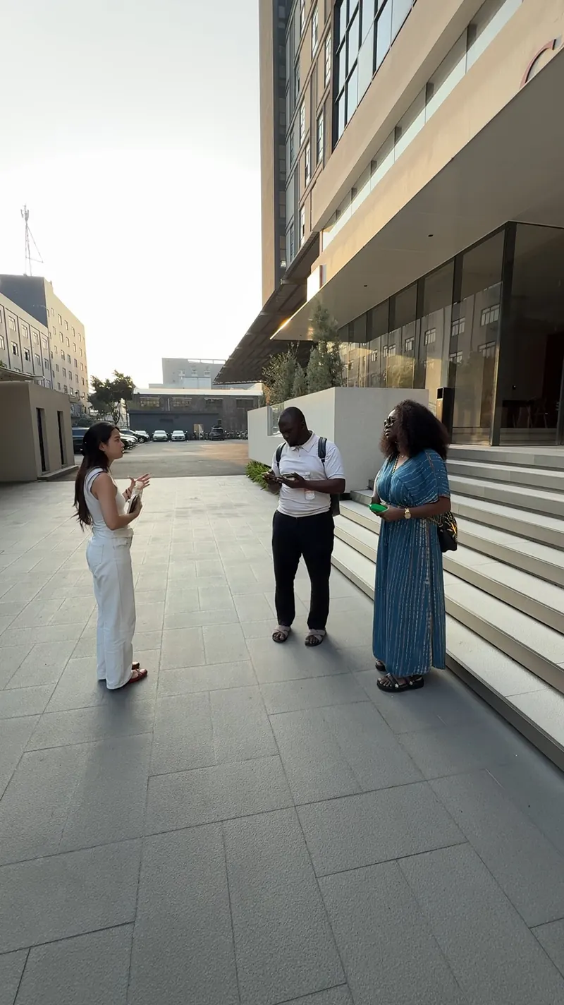 Three adults stand outside a showroom building while one gestures toward the others.