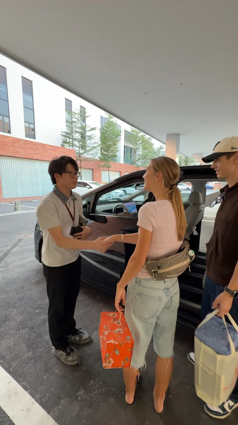 Two adults shake hands beside an open vehicle while another person stands nearby.